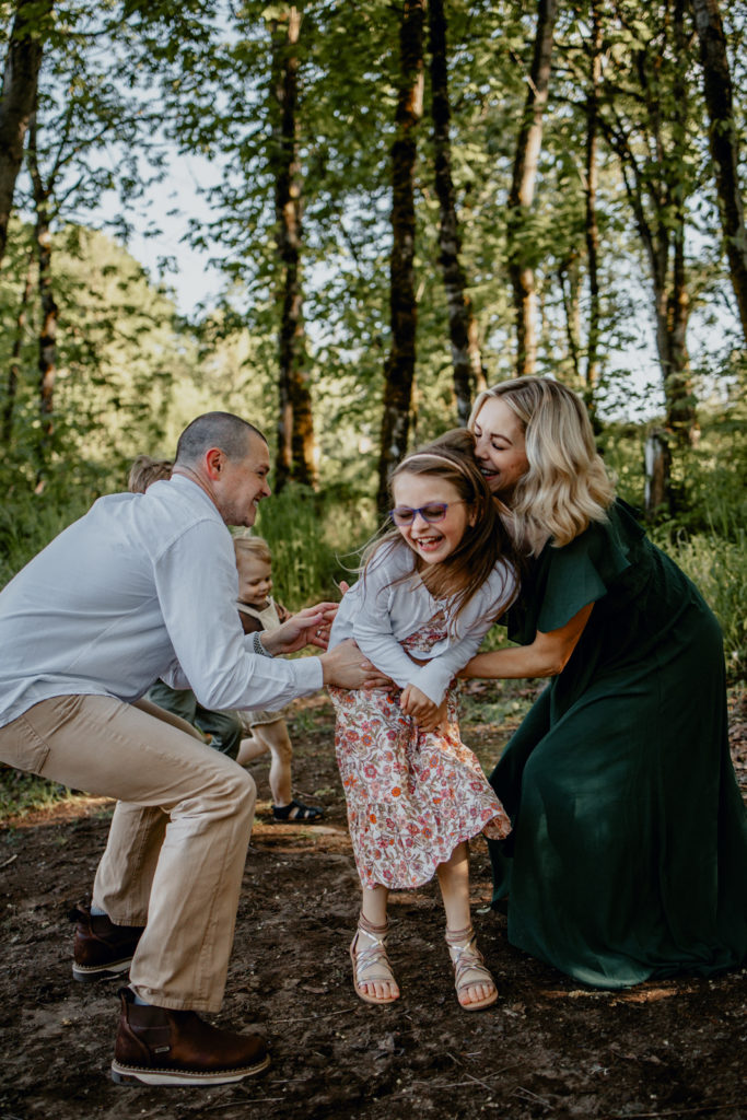 Parents tickling oldest daughter while laughing during outdoor family photography session at Armitage Park in Eugene Oregon