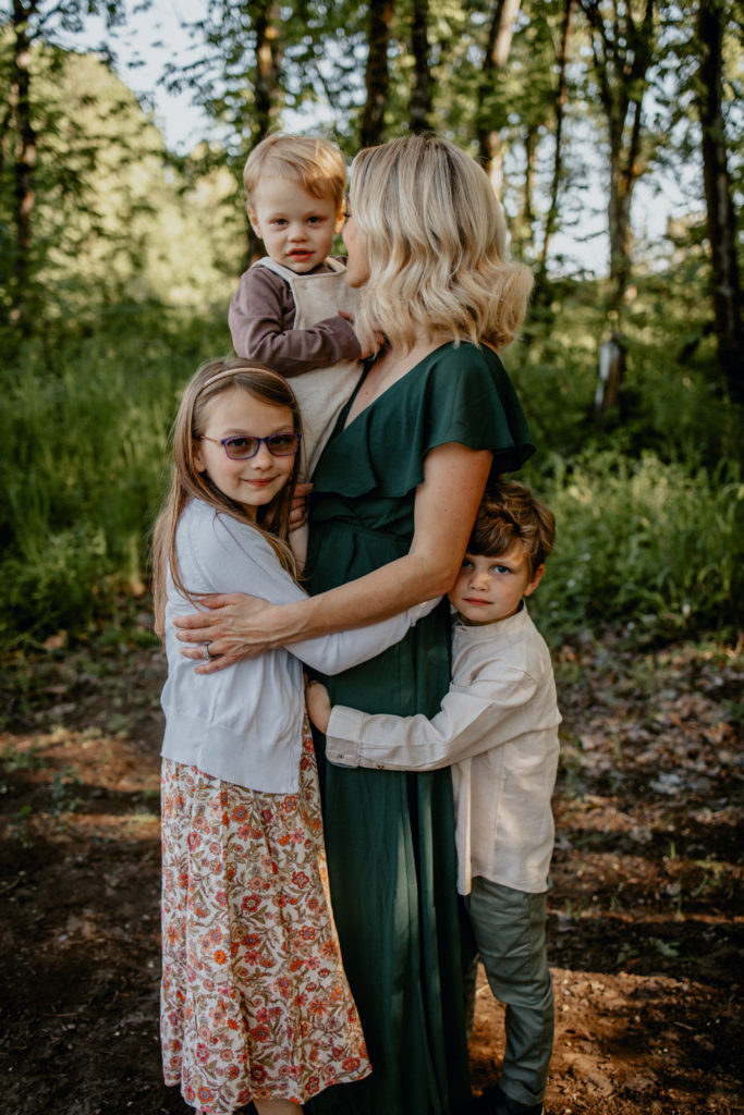 Two children hugging mom while mom holds baby during outdoor family photo session with Lux Marina Photography