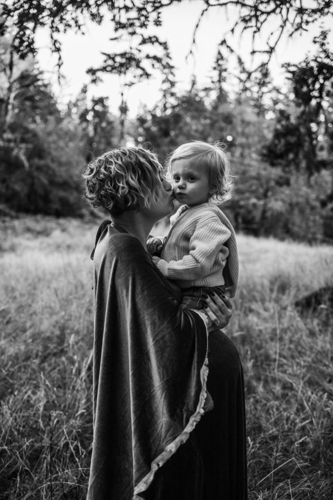Mom kissing young son as he sits on her pregnant belly during family maternity session at Spencer Butte in Eugene Oregon