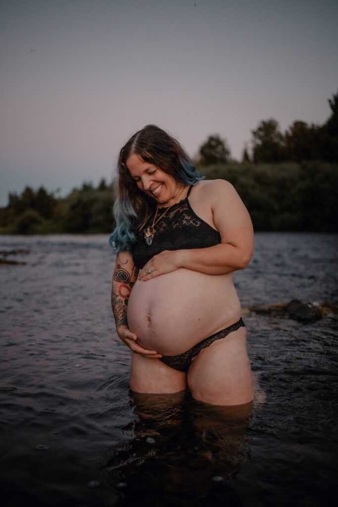 Smiling pregnant woman playing in the river during maternity session with Eugene Oregon family and birth photographer Lux Marina Photography