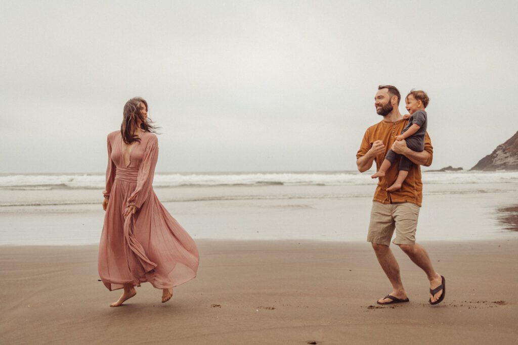 Family of three running on the Oregon Coast while they laugh and play during family photo session with Eugene, Oregon based family photographer Lux Marina Photography
