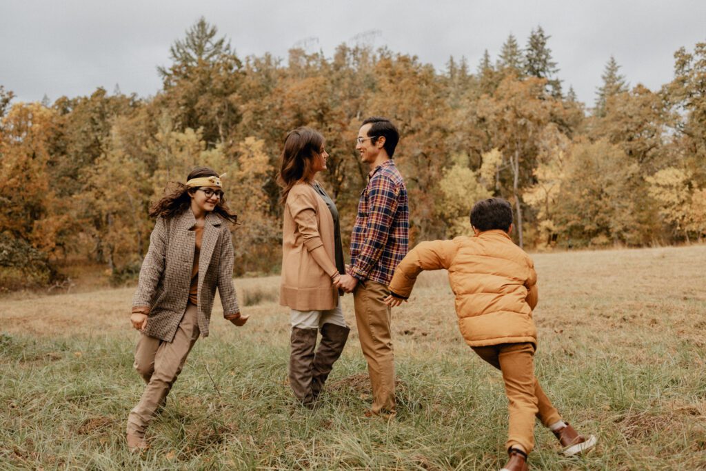 Family of four with older kids chasing each other round parents during fall family photos at Mount Pisgah in Eugene, Oregon