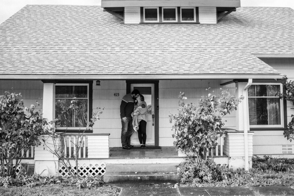 Parents holding newborn baby on their front porch after preparing their home for an in-home newborn session