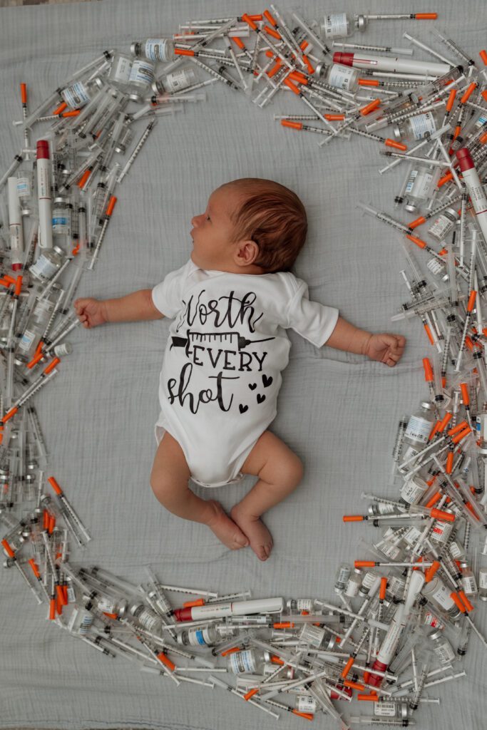 Outfit for a personalized newborn session with baby surrounded by IVF infusions and wearing white onesie saying worth every shot 