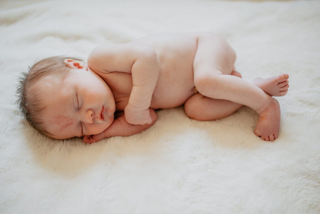 Newborn baby laying on white sheet skin as example of what to wear for newborn photos 